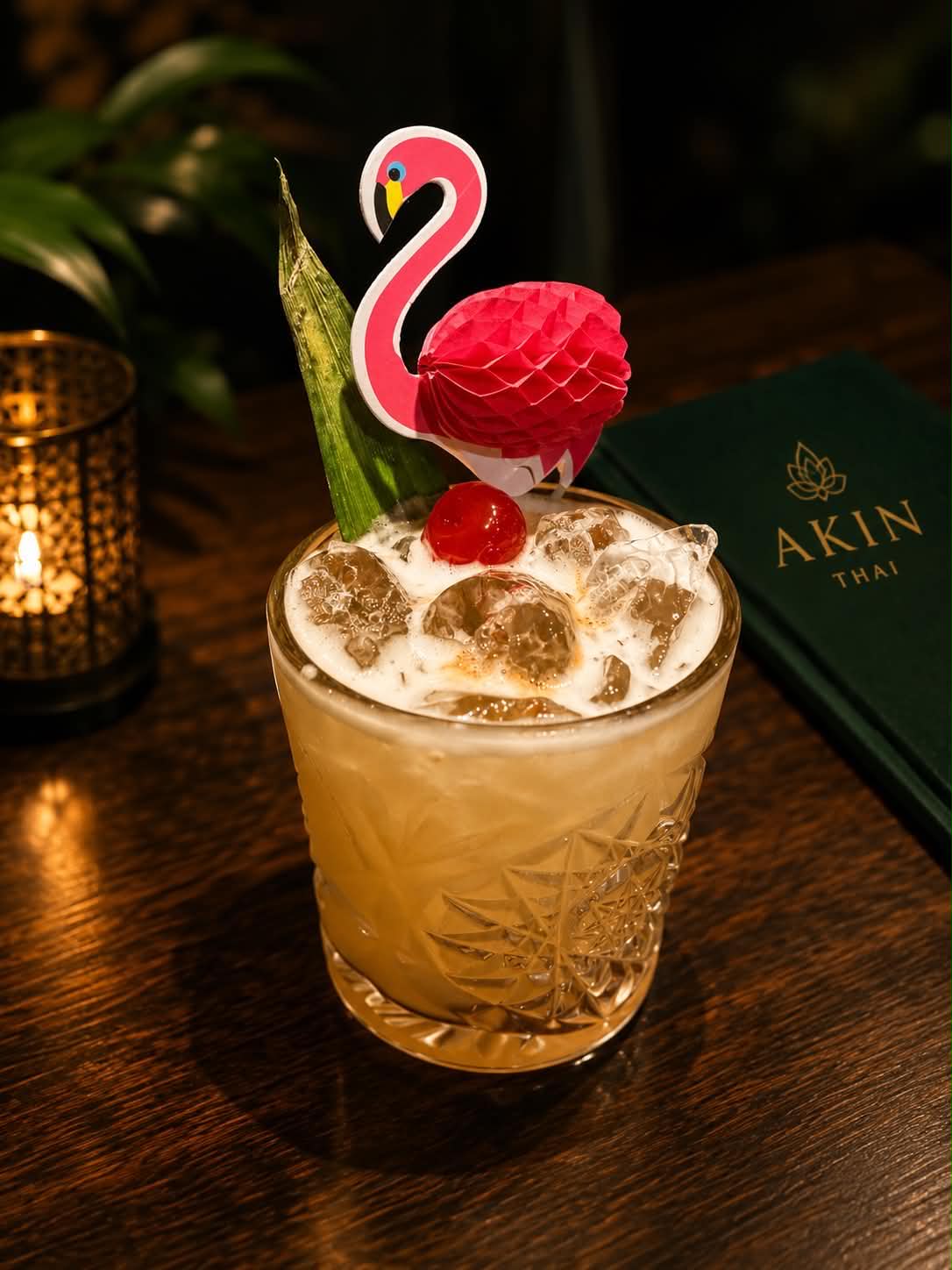 Signature cocktail with flamingo garnish beside the Akin Thai menu